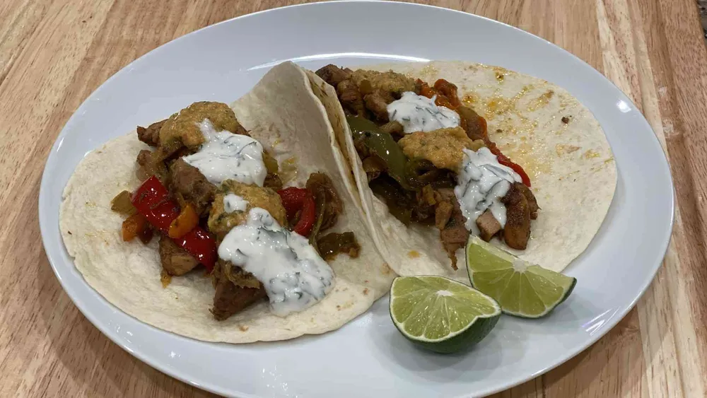 Two chicken fajitas on a plate with sliced lime