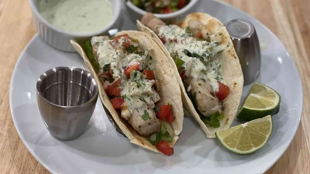 Two Hawaiian Fish tacos with lime wedges, mahi-mahi fish, creame sauce, and fresca sauce.