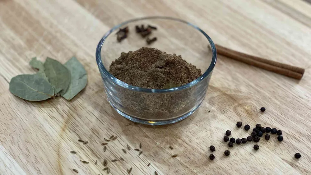 Garam Masala in a cup with ingredients used to make it on wood cutting board