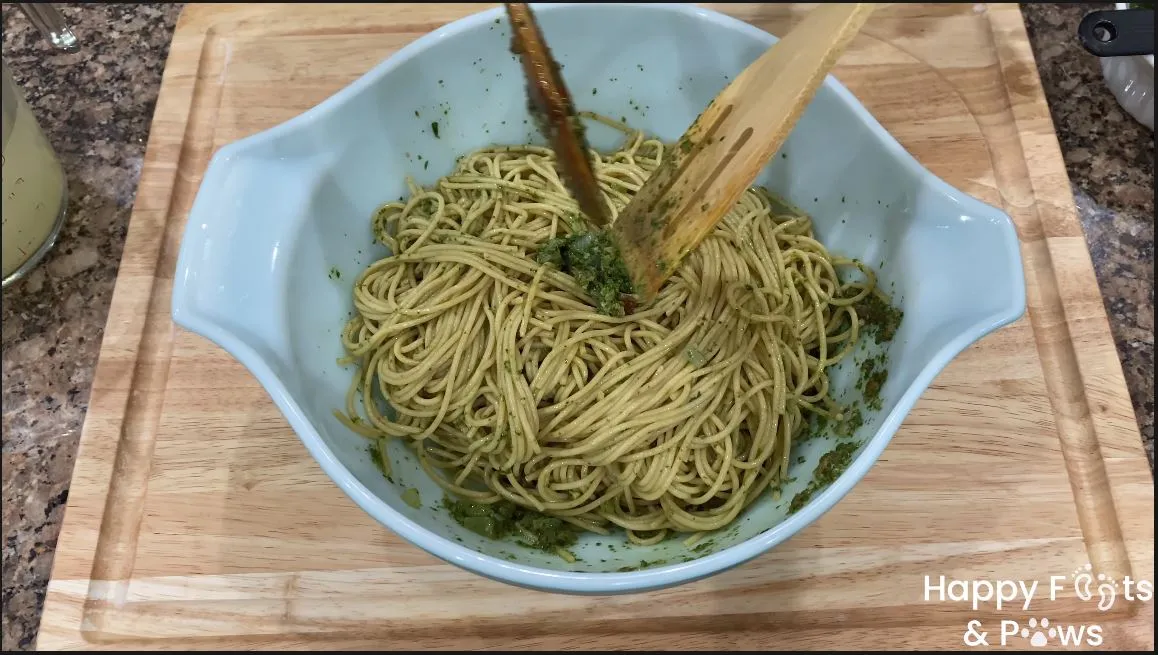 mixing noodles and pesto in a large glass bowl