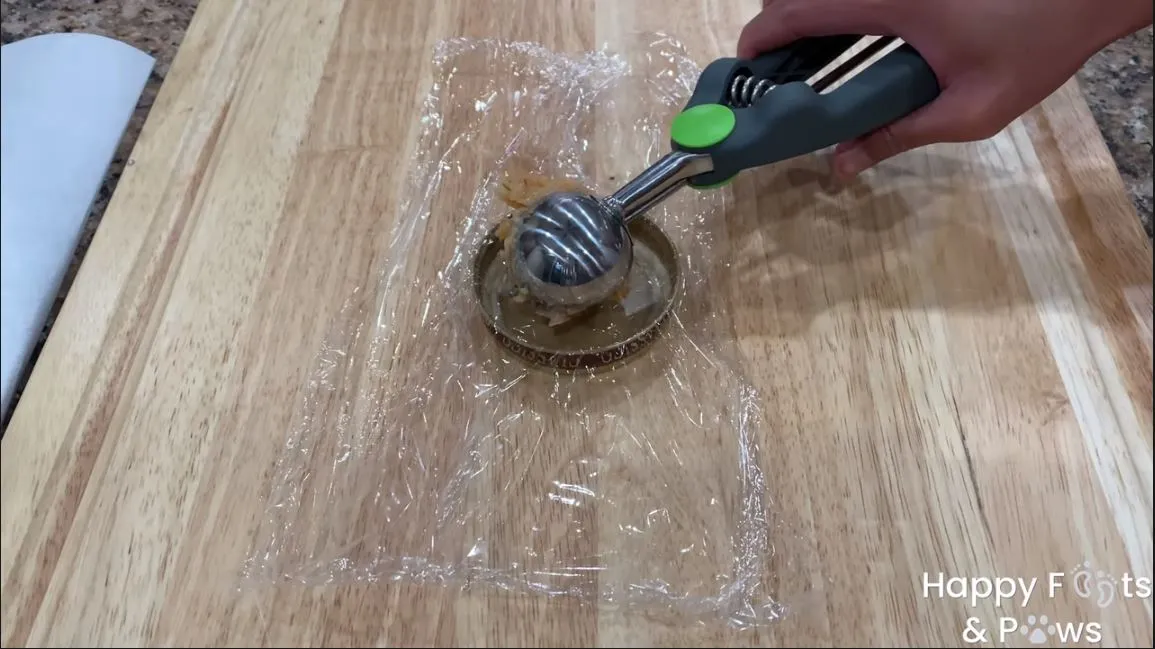 Hand with ice cream scoop placing raw shrimp cake into lid